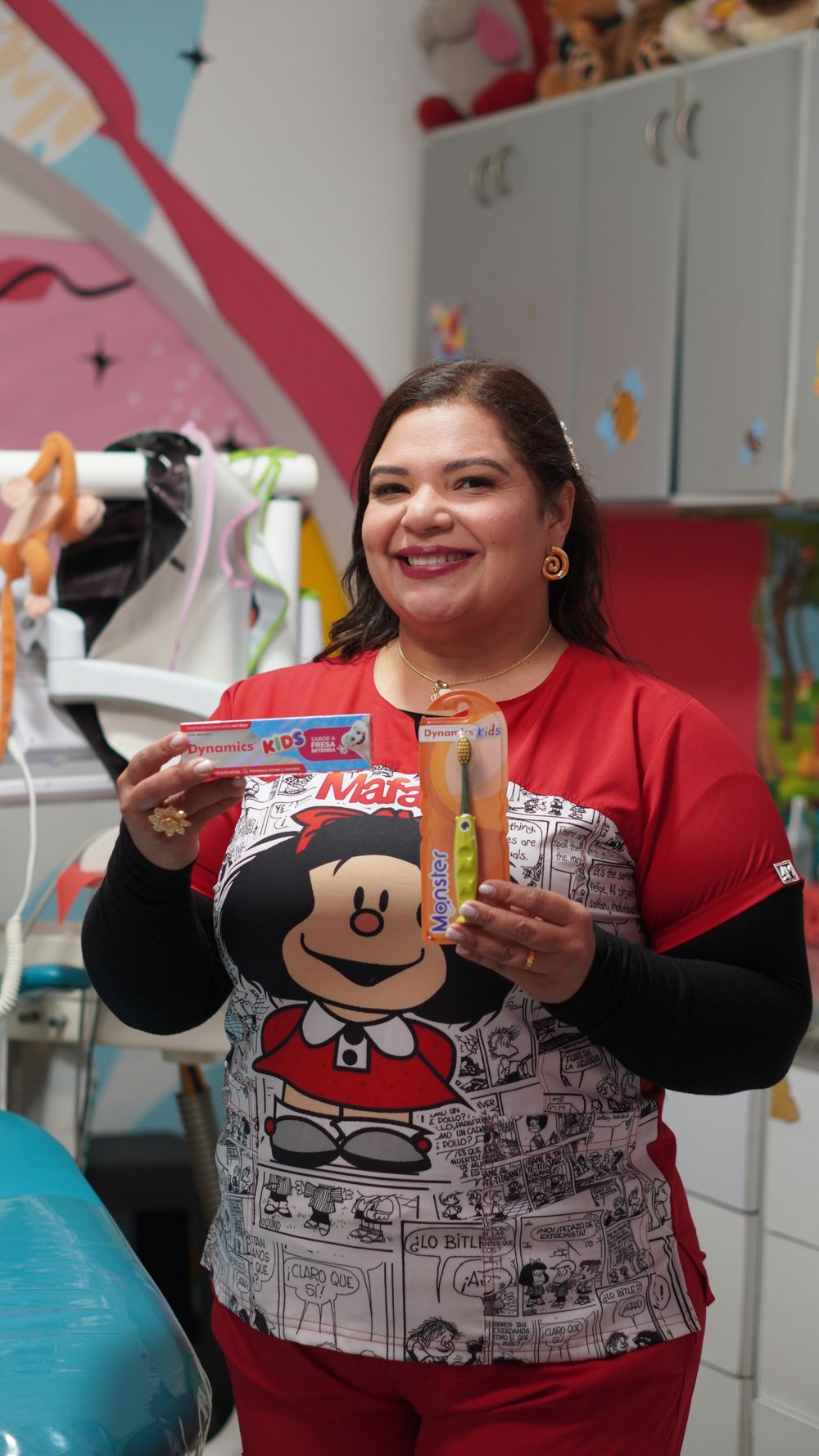 La Dra. Mine sonriendo mientras muestra una crema dental y un cepillo infantiles